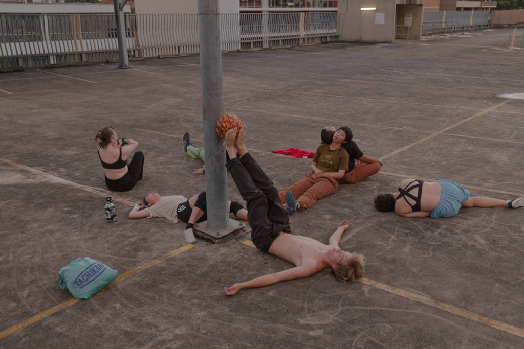 Performers posing in car park, Riana Head-Toussaint, Animate Loading 1, 2022-ongoing, Pari Ari with performers Tom Kentta, Leo Tsao, Natalie Tso, Jeremy Lowrenčev, Savannah Stimson, Bedelia Lowrenčev and Cynth Florez