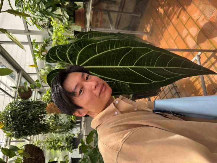 Naraphat Sakarthornsap takes a selfie with a large green leaf in a conservatory