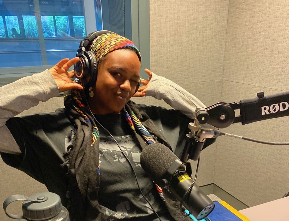 A woman in a recording studio wearing headphones smiling at the camera.