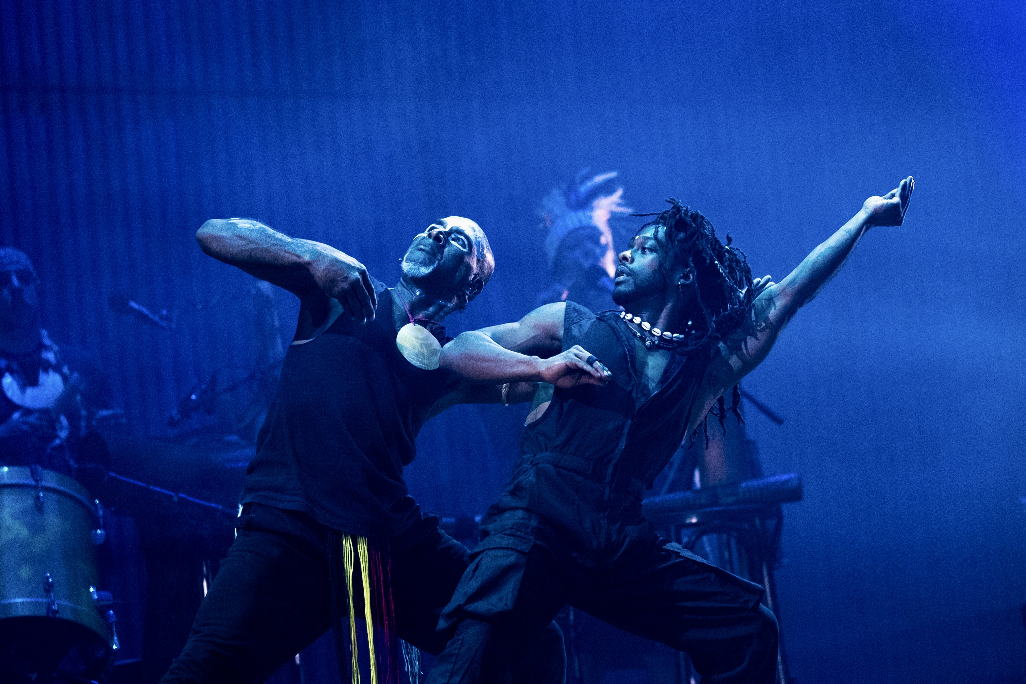 A photo of two dancers lunging side by side on stage surrounded by blue light.