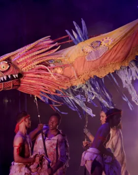 A photo of a large dragon puppet being puppeteered by five performers.