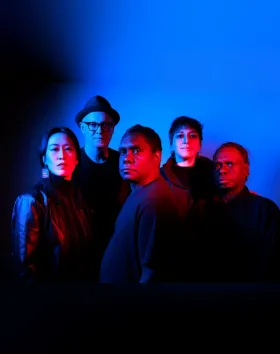 A group photo of the Hand to Earth group in dark and dramatic blue lighting.