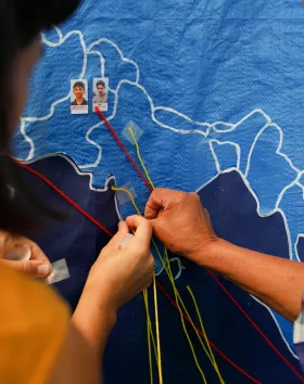 A photo of two people pining coloured string onto a map. 