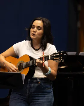 A photo of a musician in the studio holding an acoustic guitar.