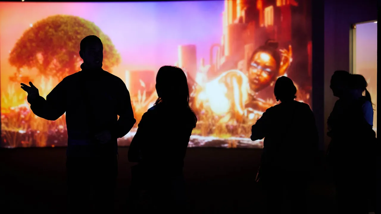 A photo of a large digital screen with the shadows of four people walking past.