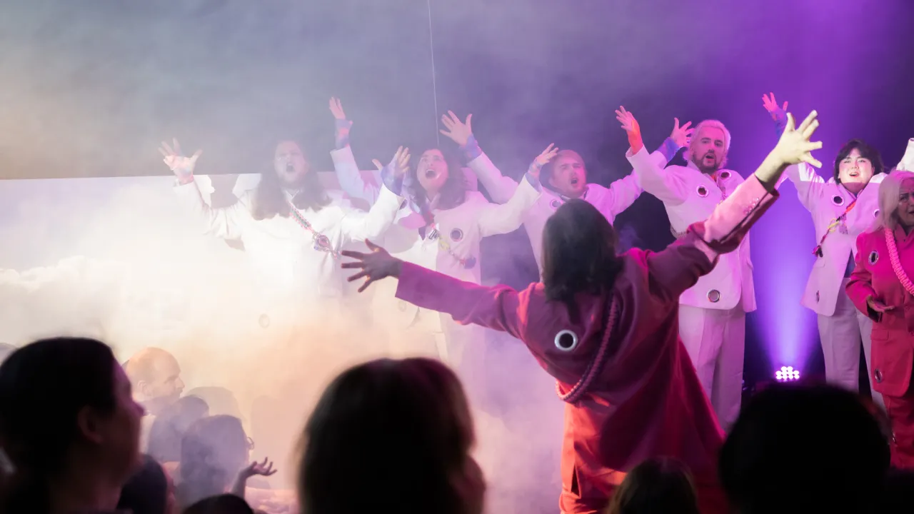 Performance at a theatre with people raising their arms and smoke.