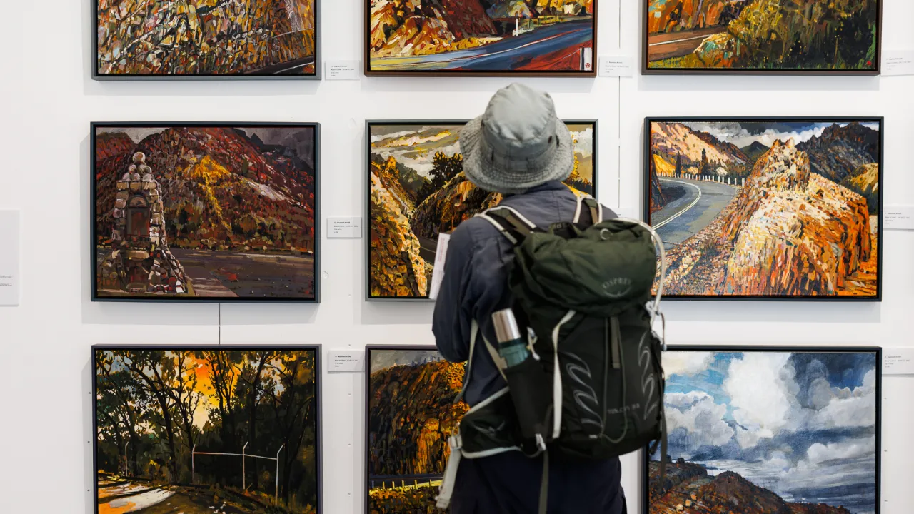 A person standing facing away from the camera in front of a white wall with nine artworks arranged in a square.