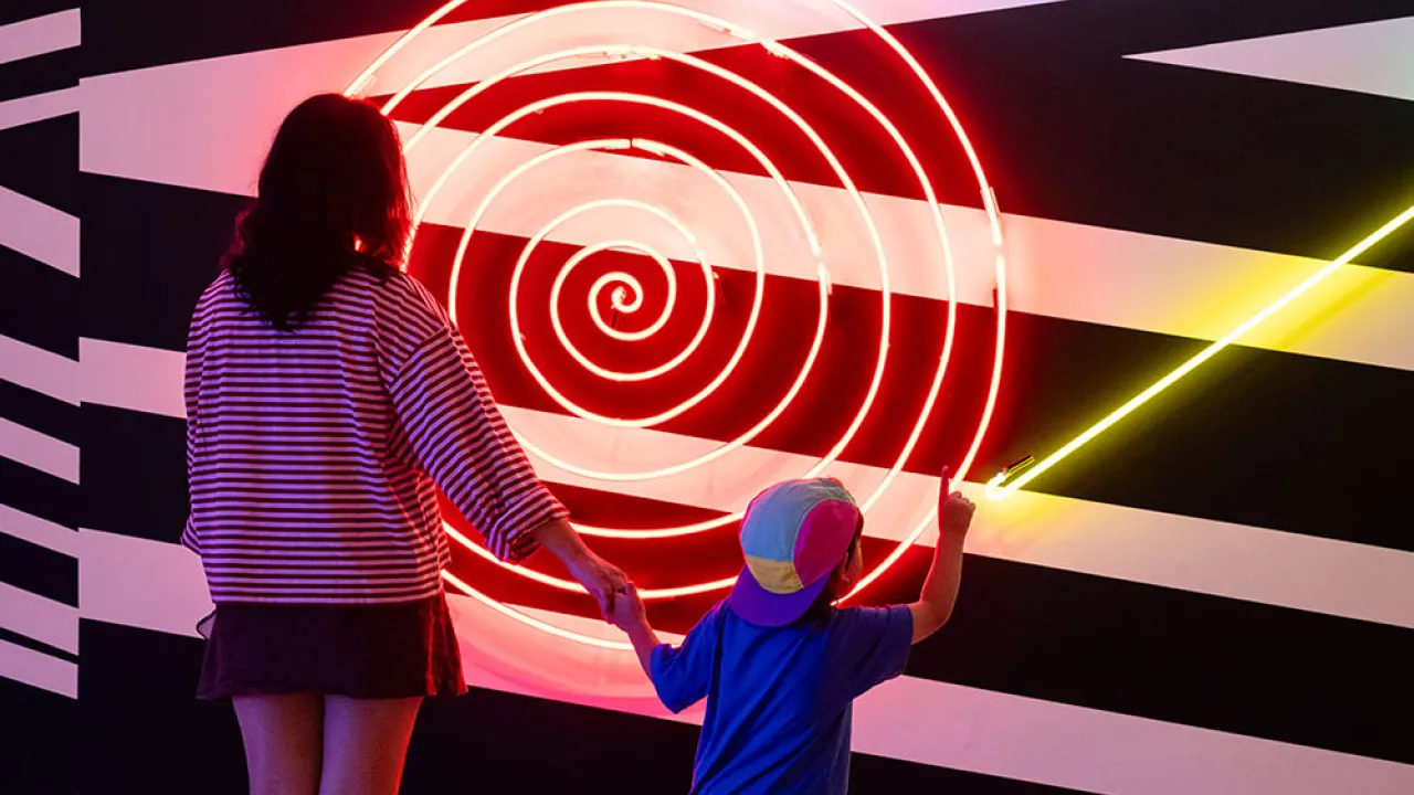 Woman and child standing in front of a neon artwork