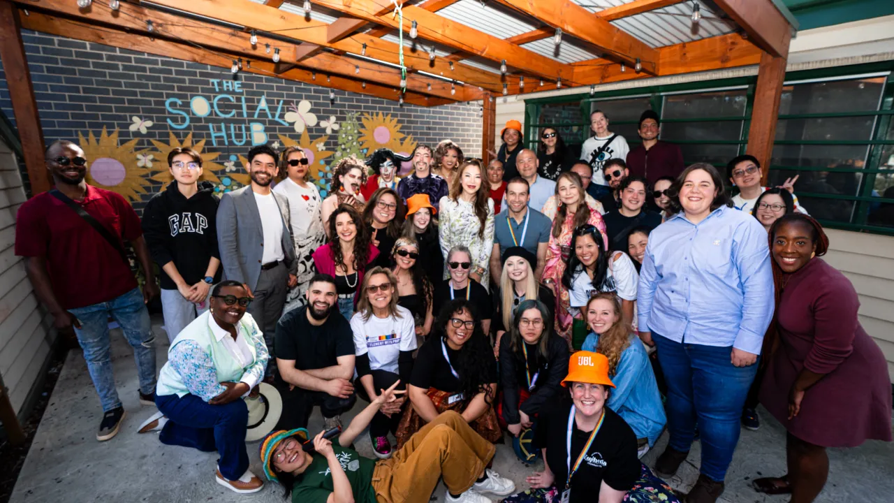 A diverse group of people gathered together for a multicultural celebration, smiling and standing side by side. The group reflects a range of cultural backgrounds, ages and identities, capturing a sense of community, connection and belonging.
