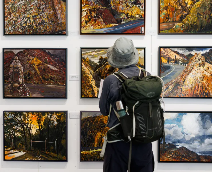 A person standing facing away from the camera in front of a white wall with nine artworks arranged in a square.