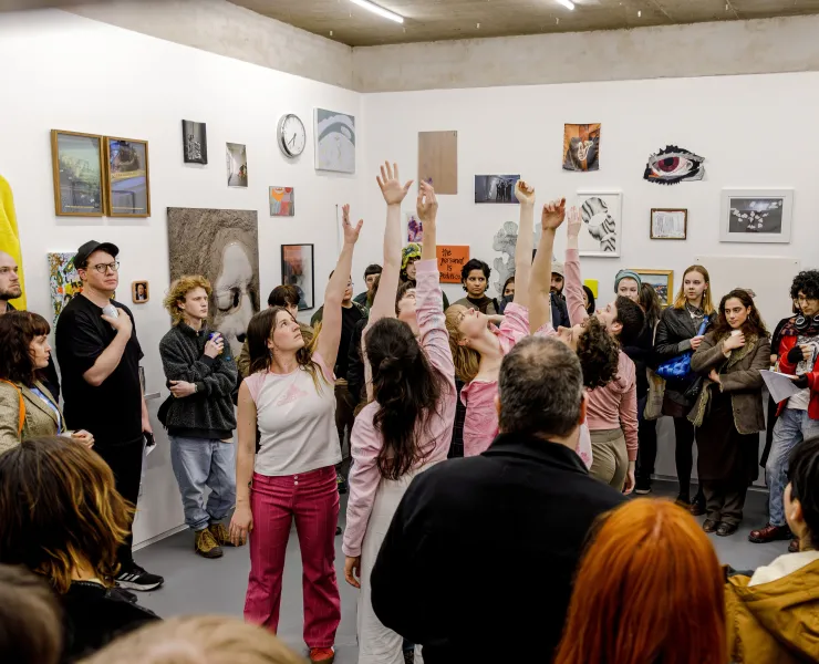 A photo of a circle of dancers facing each other with their arms up in the air. A large crowd surround them watching.