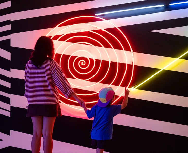 Woman and child standing in front of a neon artwork