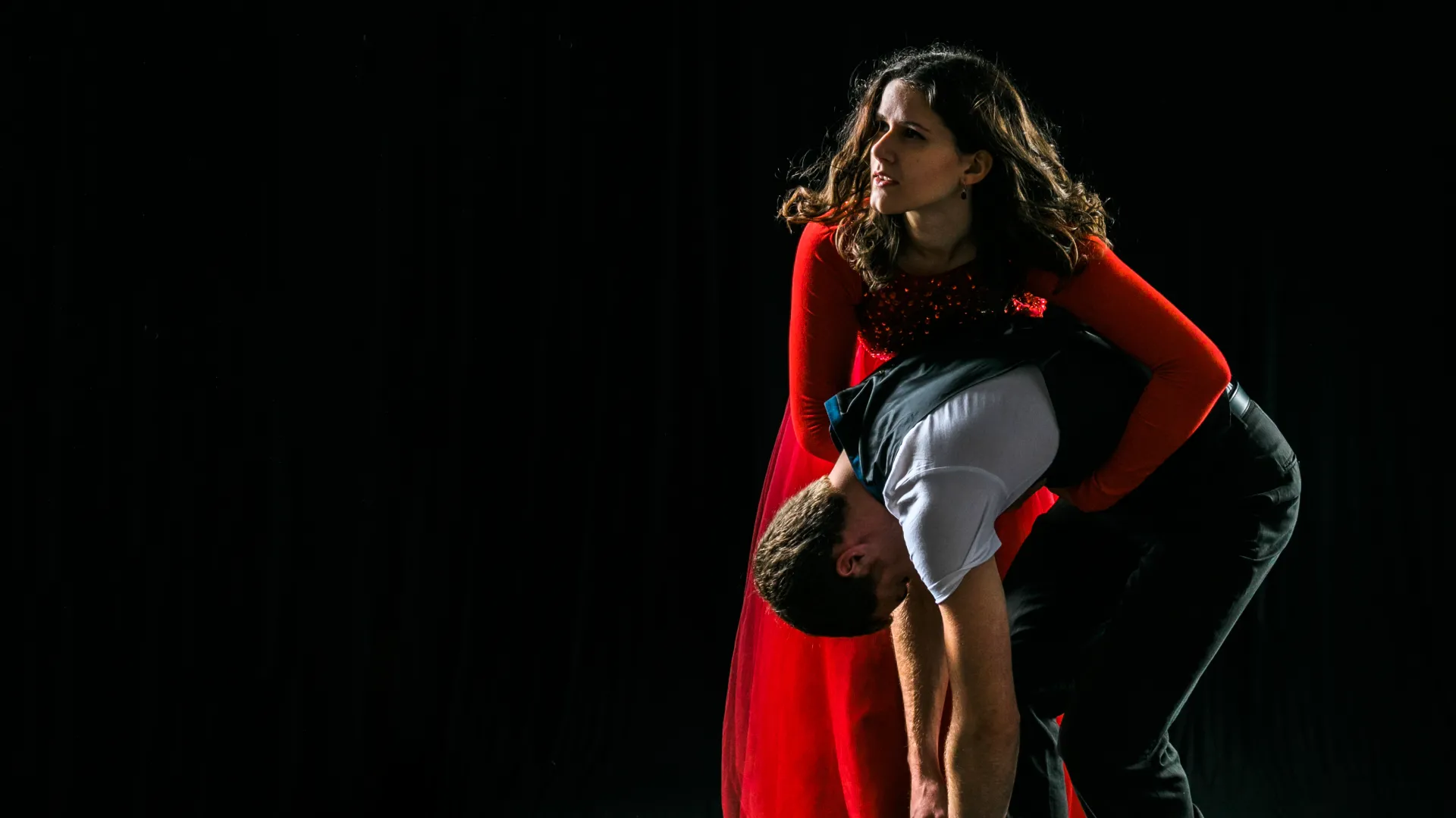 Woman in red dress holding man in dark clothes on black background